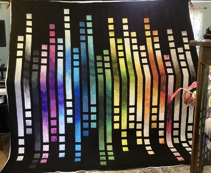 a colorful quilt hanging on a wall in a room with other furniture and decor items