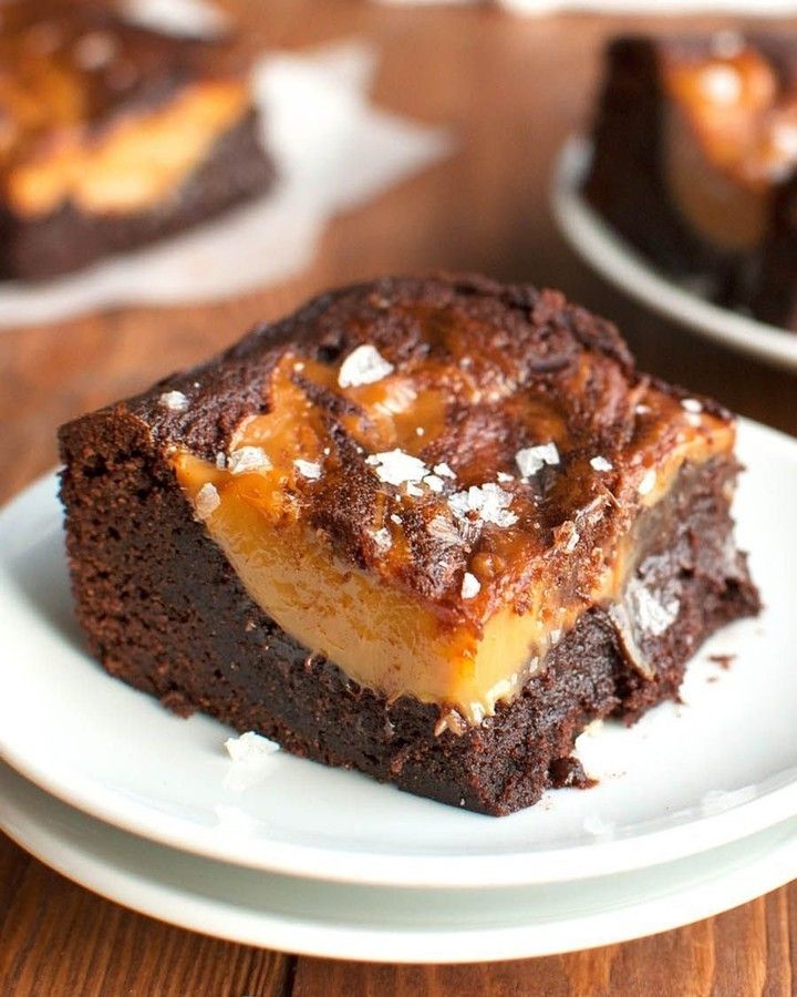 two pieces of brownie with caramel topping on a white plate next to another piece of cake