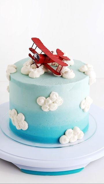 a blue and white cake with a red airplane on it's top, sitting on a plate