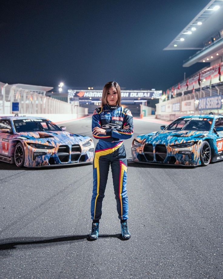 a woman standing in front of two racing cars on a race track at night time