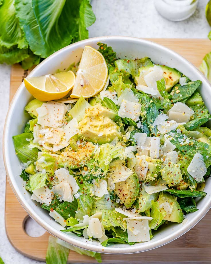 a white bowl filled with lettuce and lemon wedges on top of a cutting board