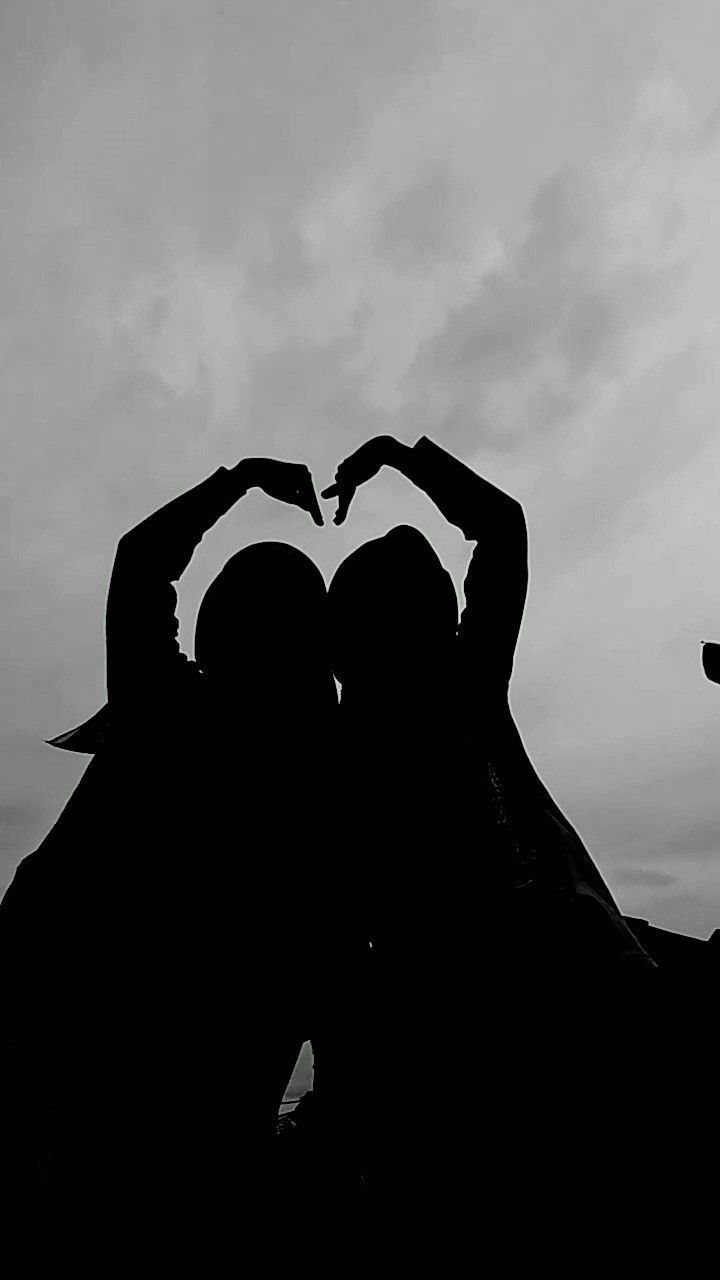 two people making a heart shape with their hands in front of the camera, against a cloudy sky