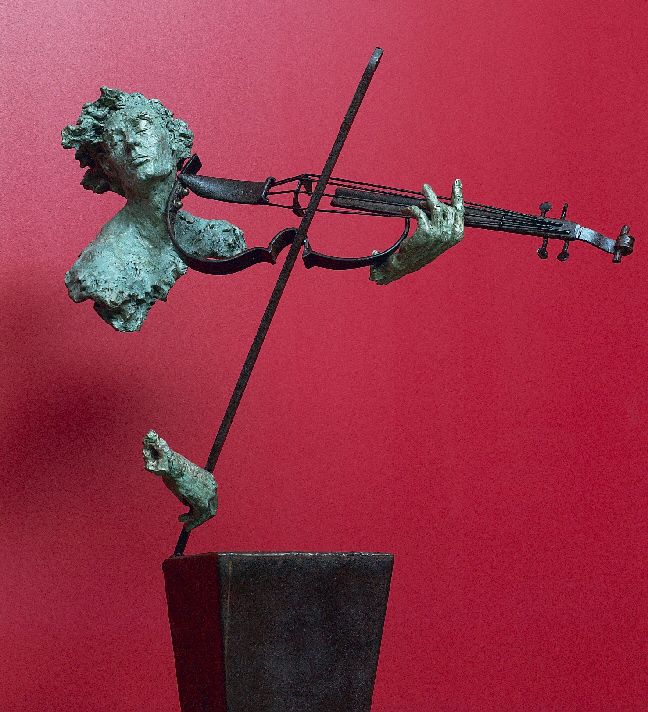 a statue of a man playing the violin in front of a red wall with a black vase