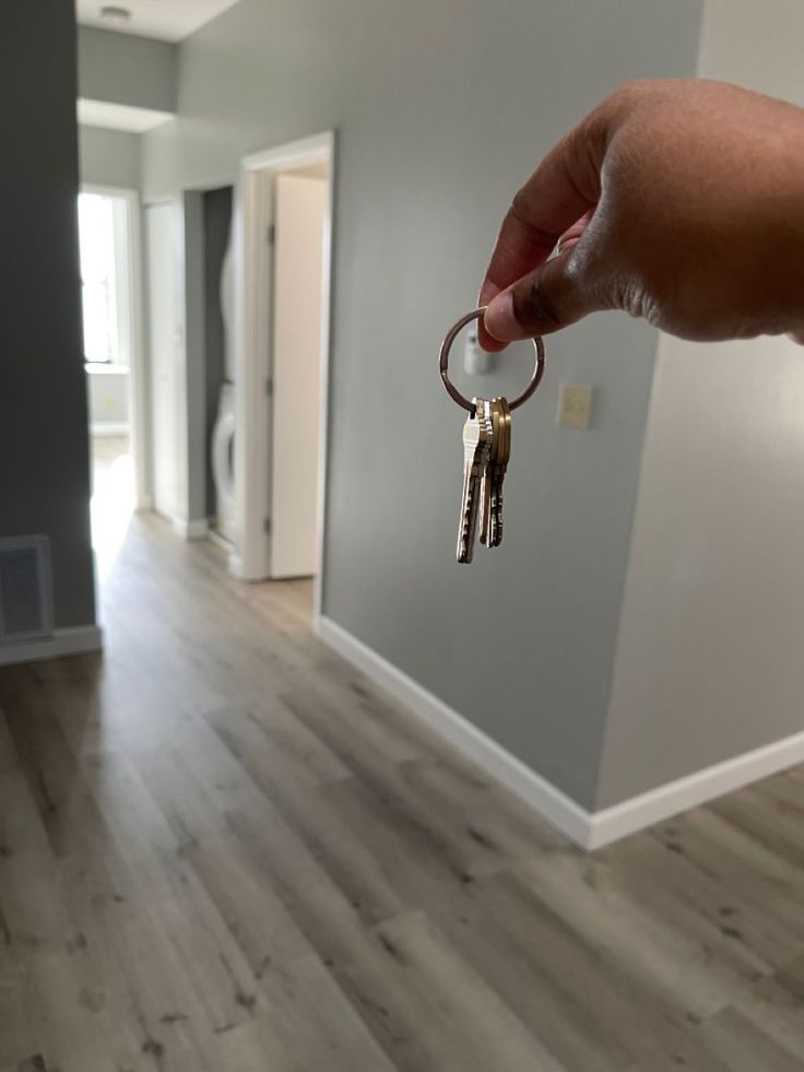 a hand is holding keys in the middle of a room with hardwood floors and gray walls