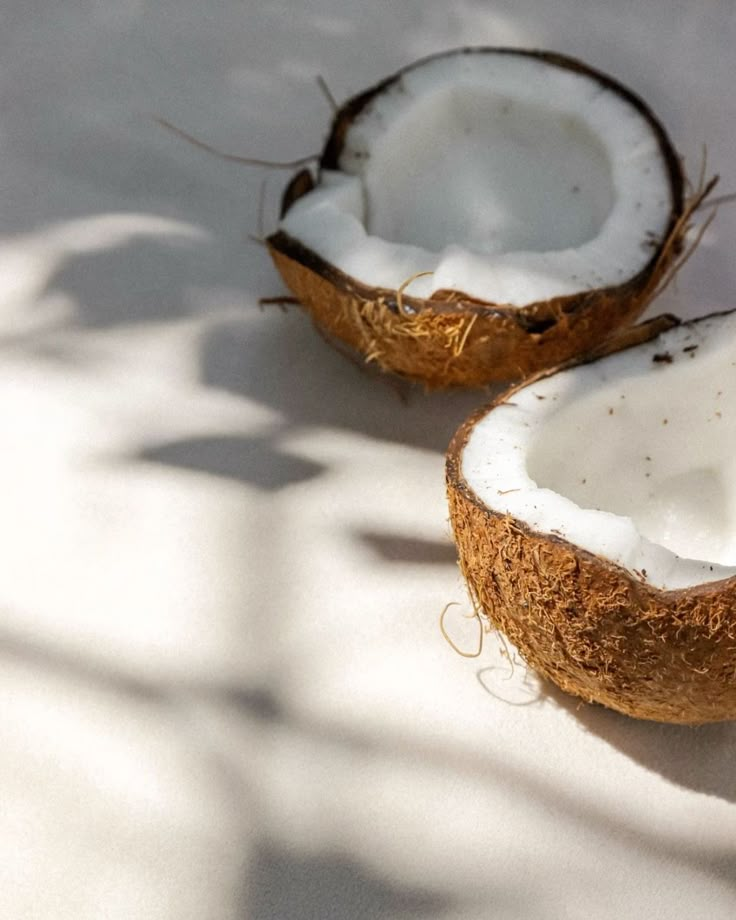 two coconuts sitting on top of a white surface next to each other with one cut in half