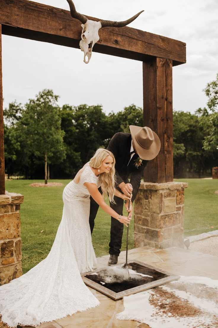 a bride and groom standing in front of an outdoor fire pit with a cow skull on the wall