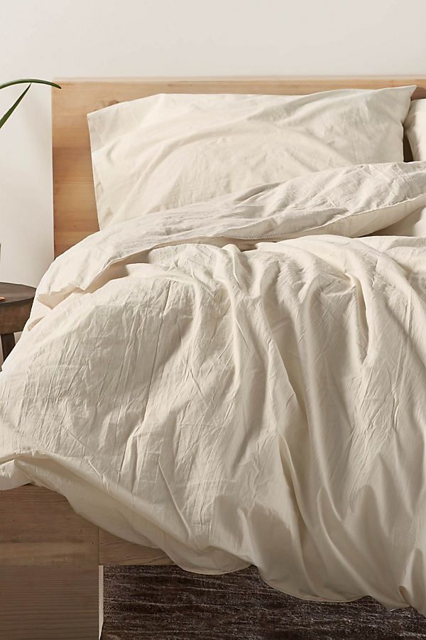 an unmade bed with white linens and a plant next to it on a wooden headboard