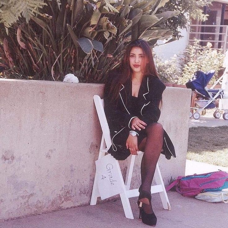 a woman sitting on top of a white chair next to a plant