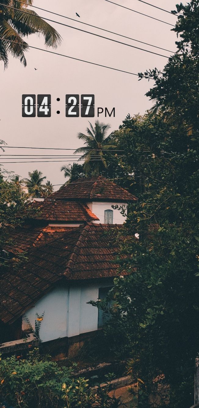 an old house with the time displayed on it's roof in front of palm trees