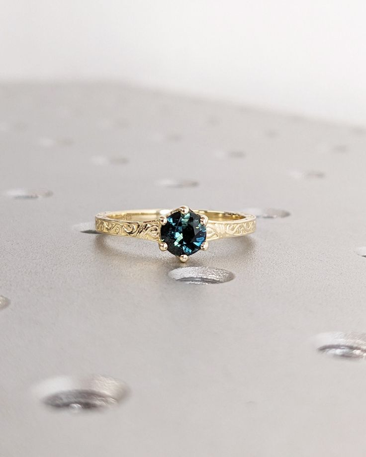 a gold ring with a blue stone on it sitting on top of a silver surface