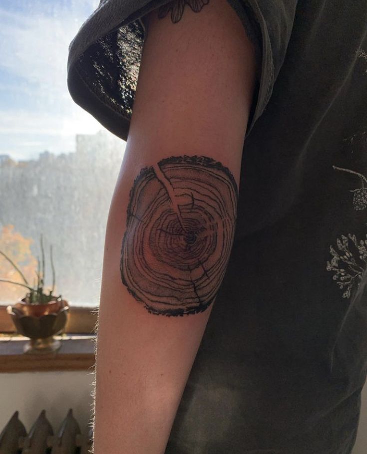 a man with a tattoo on his arm holding a knife in front of a tree stump