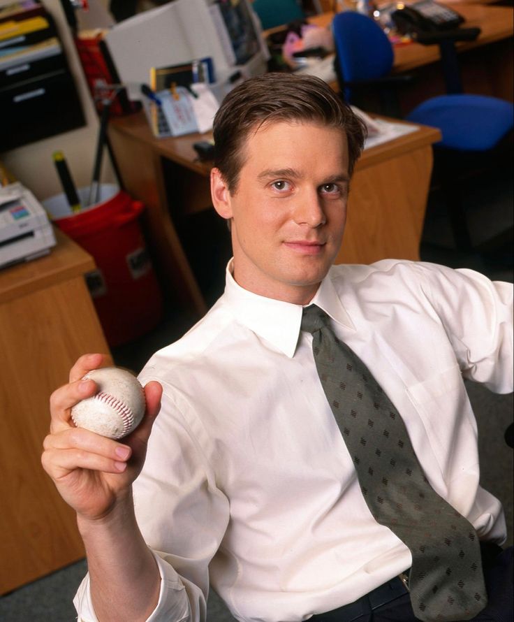 a man in a white shirt and tie holding up a baseball with a ball on it