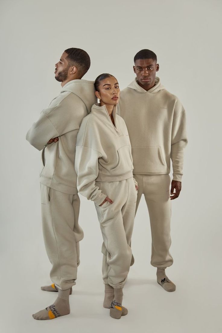 two men and a woman standing in front of a white background wearing beige sweat suits