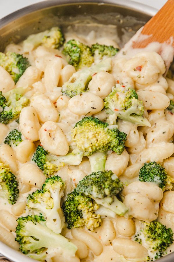 broccoli and macaroni are being stirred with a wooden spoon