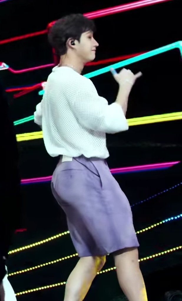 a male in a white shirt and purple skirt is dancing with neon lights behind him