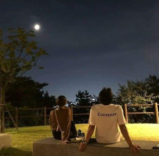 two people sitting on a bench watching the moon