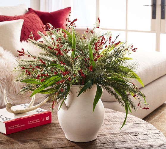 a white vase filled with red flowers on top of a wooden table next to a couch