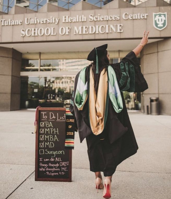 a woman in graduation gown and cap walking towards the school of medicine building with her hand up