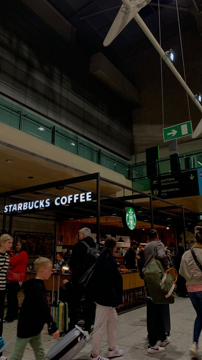 people are walking through an airport terminal with their suitcases and coffee bags hanging from the ceiling