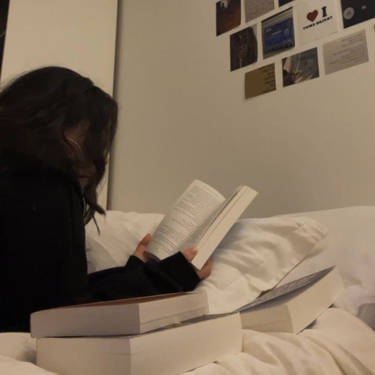 a woman reading a book on top of a bed in a room with white sheets