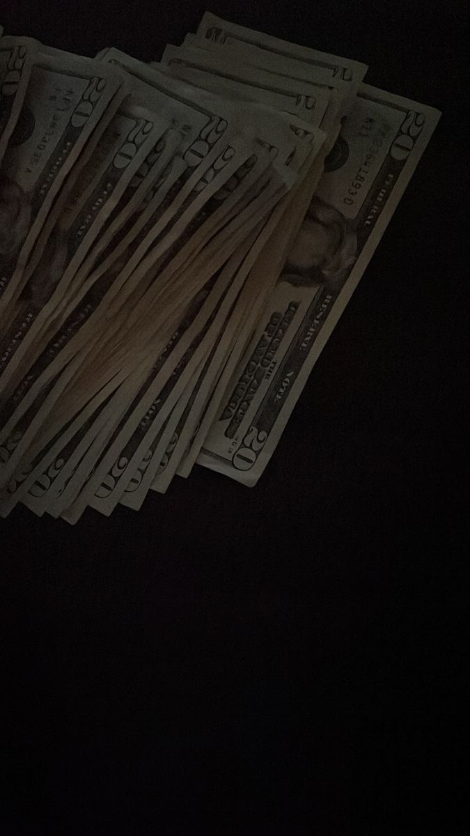 a pile of twenty dollar bills sitting on top of a black table next to a cell phone