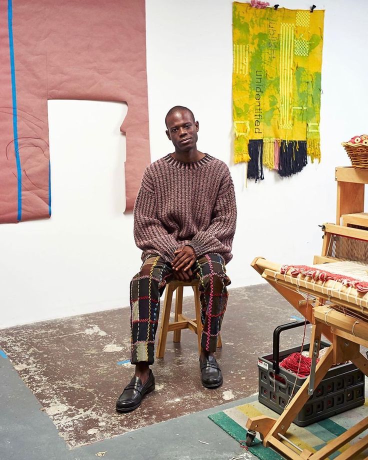 a man sitting on top of a wooden chair in front of a painting easel