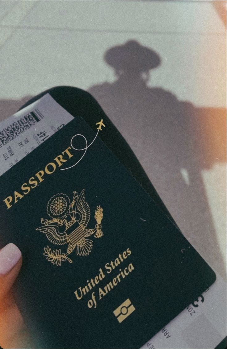 a person holding up a passport in their hand with the shadow of a man behind them