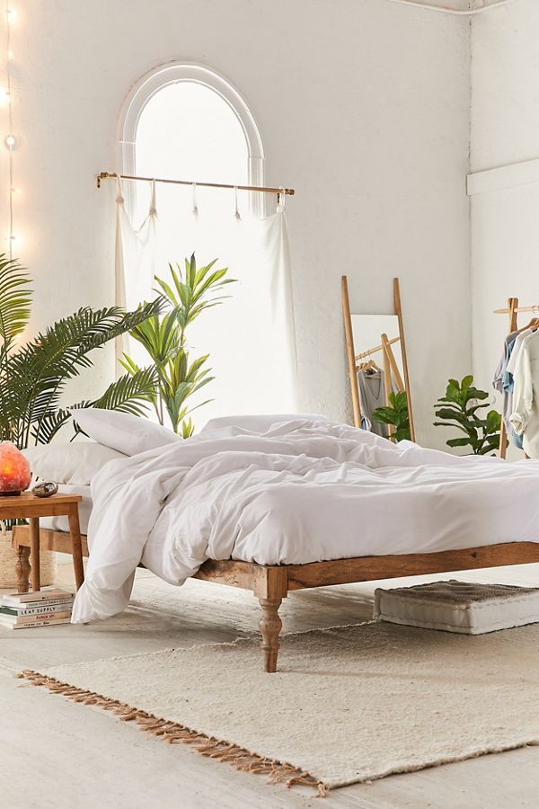 a bed with white sheets and pillows in a room next to a mirror, potted plant and other items