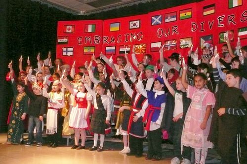 a group of children standing in front of a red wall holding up their hands and waving