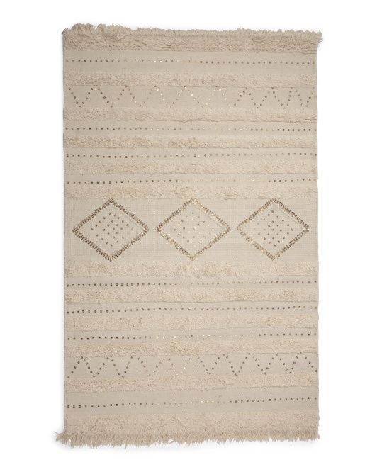 a beige rug with diamond shapes and fringes on the bottom, in front of a white background