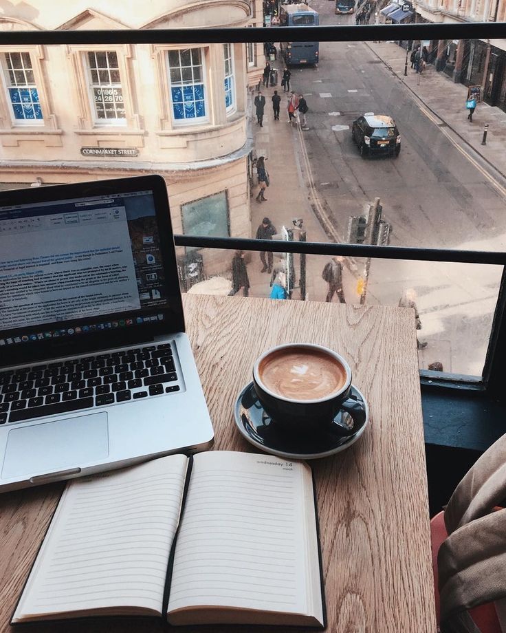 a laptop computer sitting on top of a wooden table next to a cup of coffee