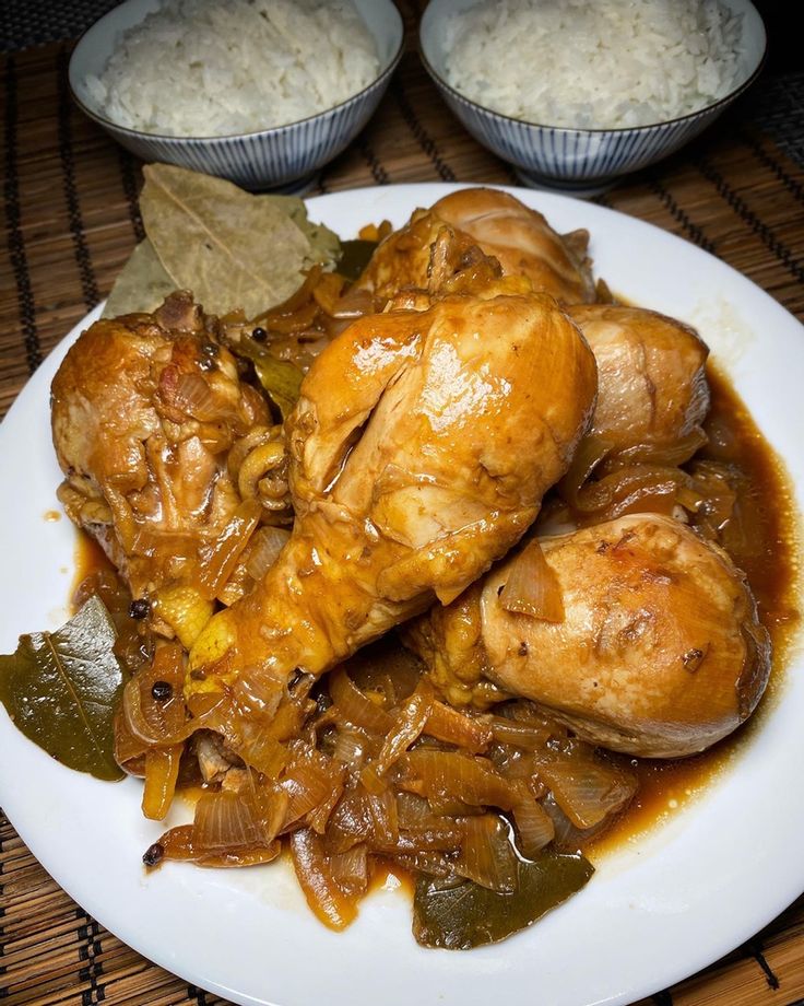 a white plate topped with chicken covered in gravy next to bowls of rice