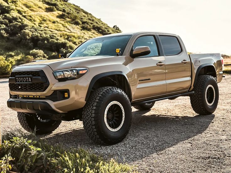 a tan toyota pickup truck parked on top of a gravel road next to trees and bushes