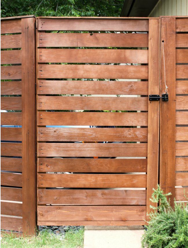 a wooden gate in front of a house with grass and bushes growing on the side