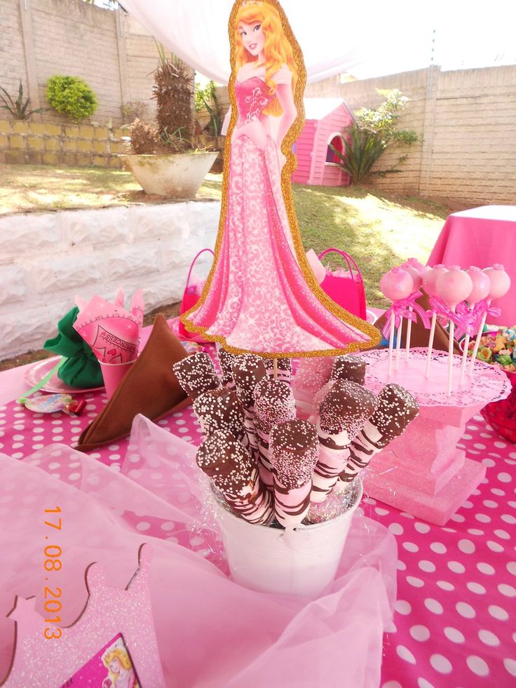 a pink table topped with cake pops and princess figurines