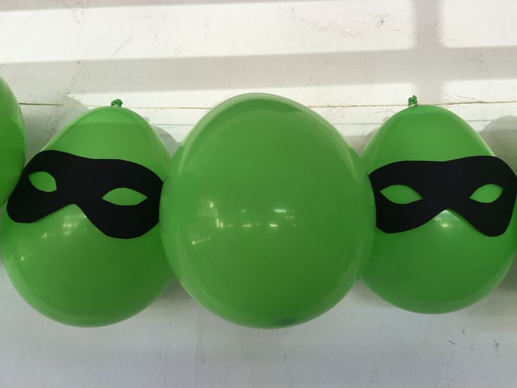 three green balloons with masks on them are lined up in a row against a white wall