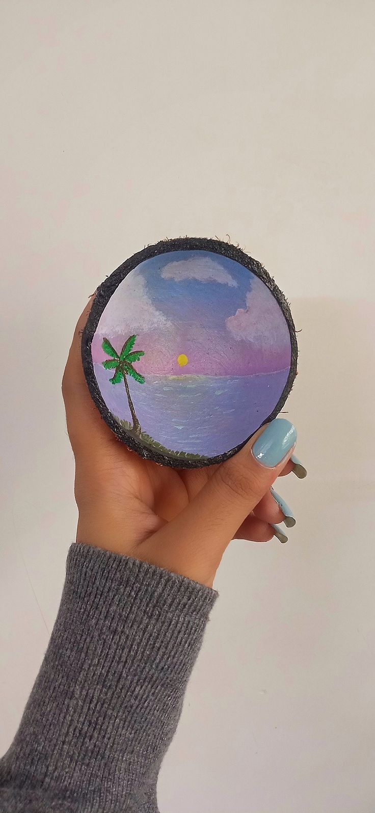 a person holding up a small mirror with a palm tree on the beach in it