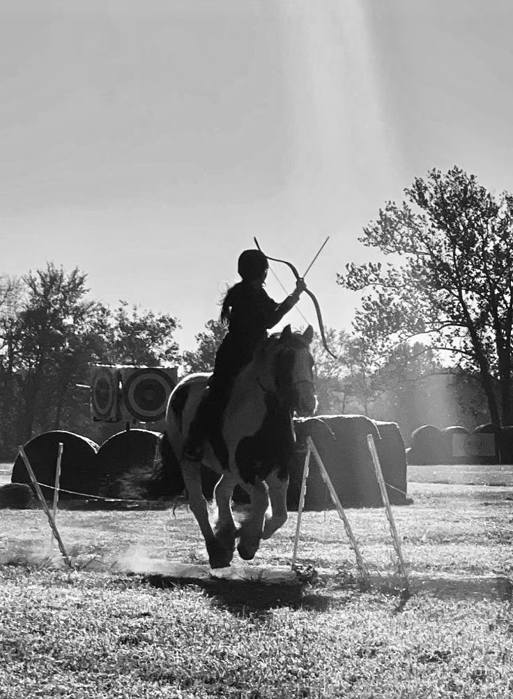 a man riding on the back of a white and black horse holding a bow in his hand