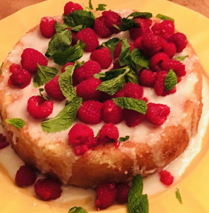 a dessert with raspberries and mint leaves on it sitting on a yellow plate