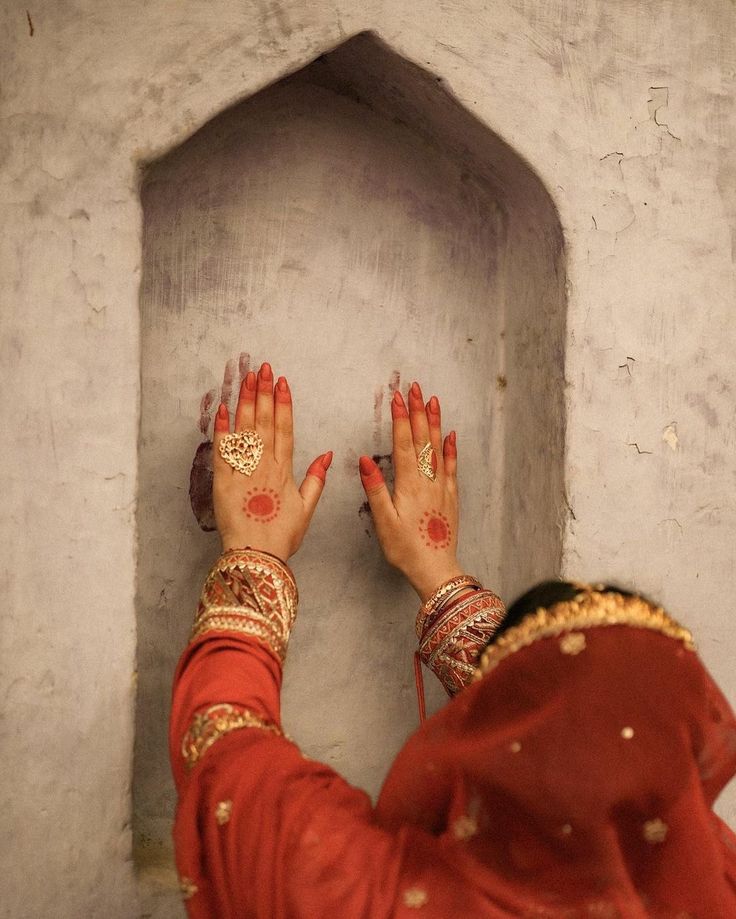 a woman with her hands up in front of a stone wall and doorway, wearing red sari