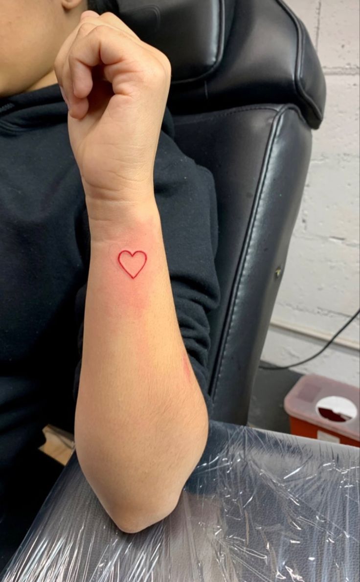 a woman with a small heart tattoo on her arm sitting at a desk in front of a computer