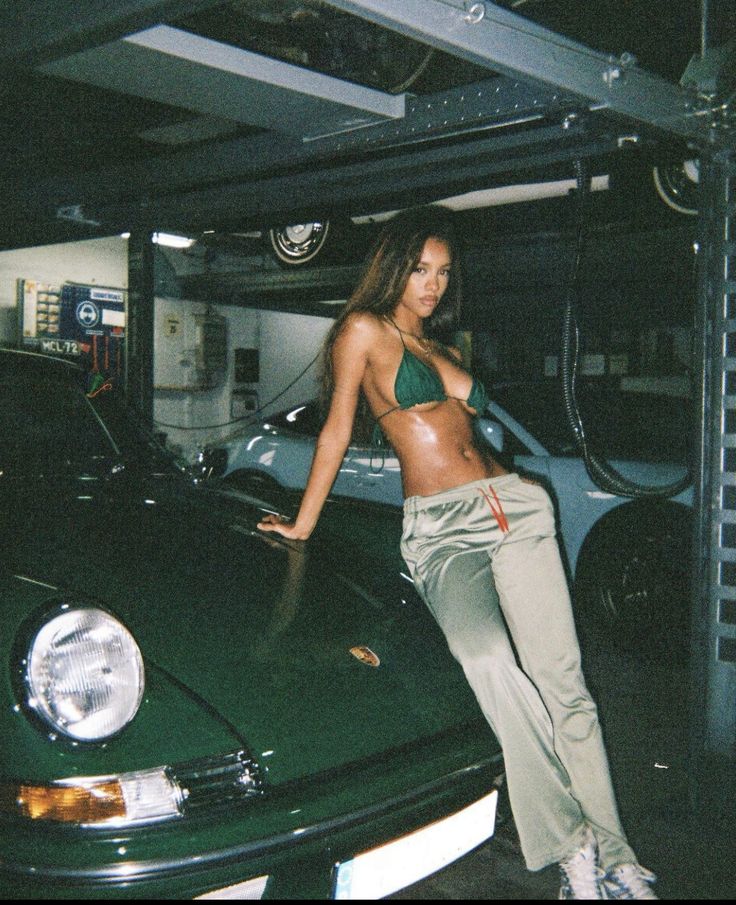 a woman leaning on the hood of a green sports car in a garage with other cars