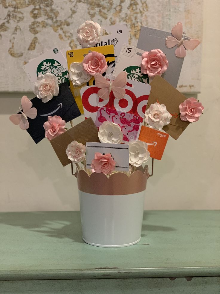 a cup with flowers and cards in it on a table next to a window sill