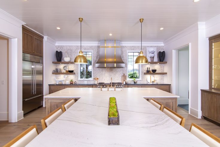 a large kitchen with marble counter tops and gold pendant lights hanging from the ceiling over the island