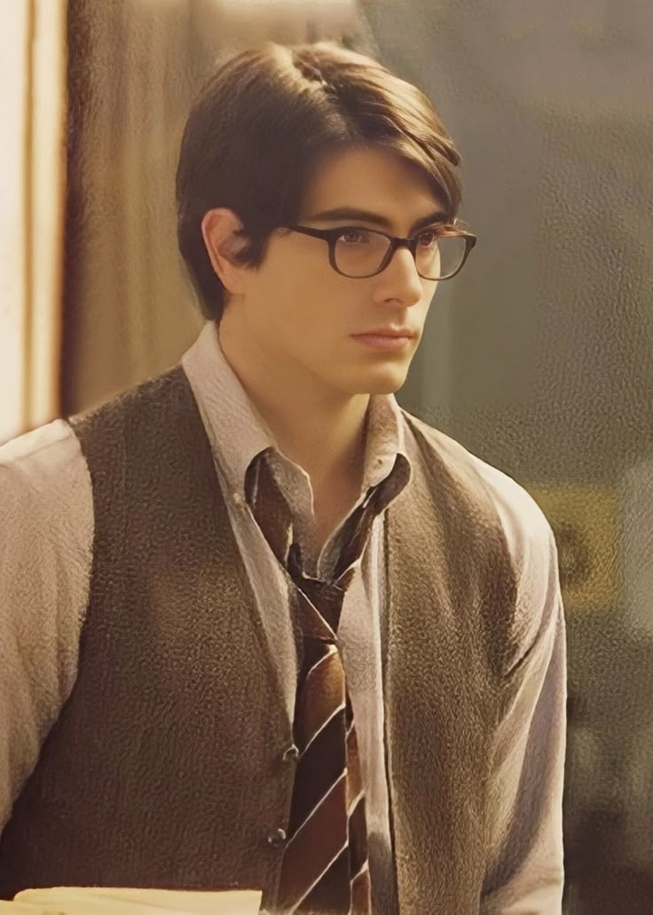 a young man wearing glasses and a tie sitting at a desk in front of a window