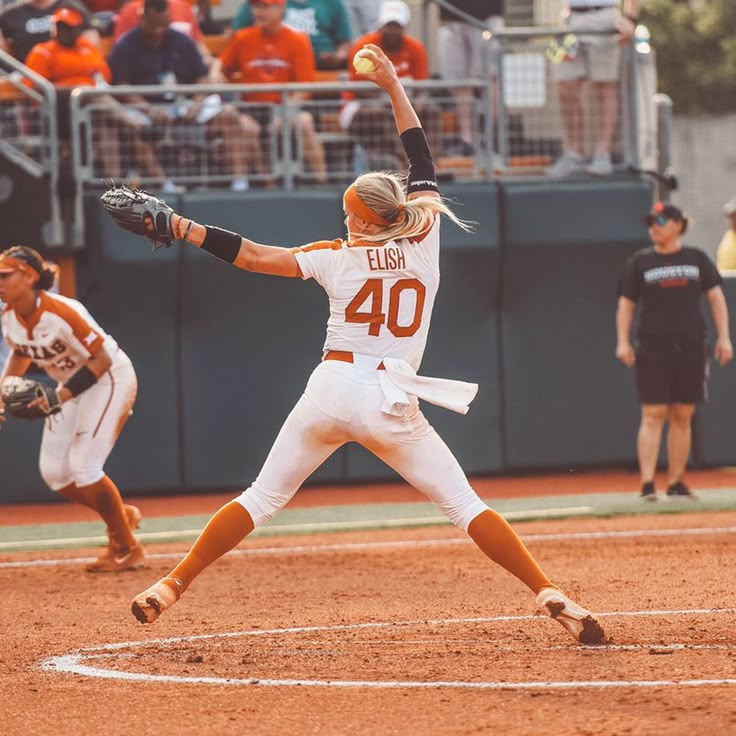 a female baseball player pitching a ball on top of a field in front of an audience