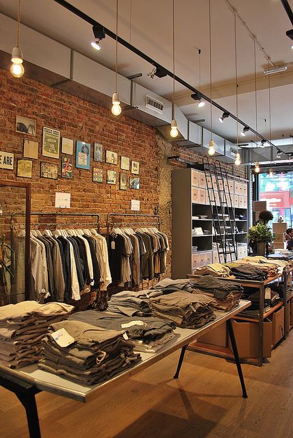 a clothing store with lots of clothes on racks and lights hanging from the ceiling above