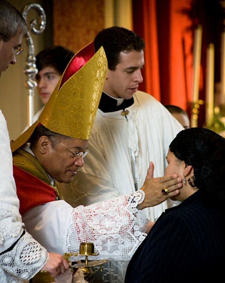 a priest is greeting a woman with her hand and other people are standing around him