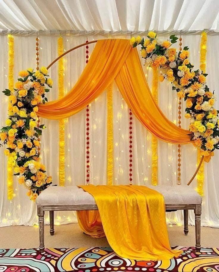 a decorated stage with yellow drapes and flowers on the wall, along with a white bench