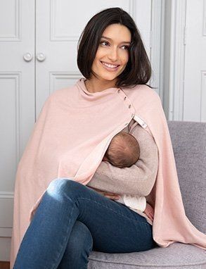 a woman sitting on a couch holding a baby wrapped in a pink blanket and smiling at the camera